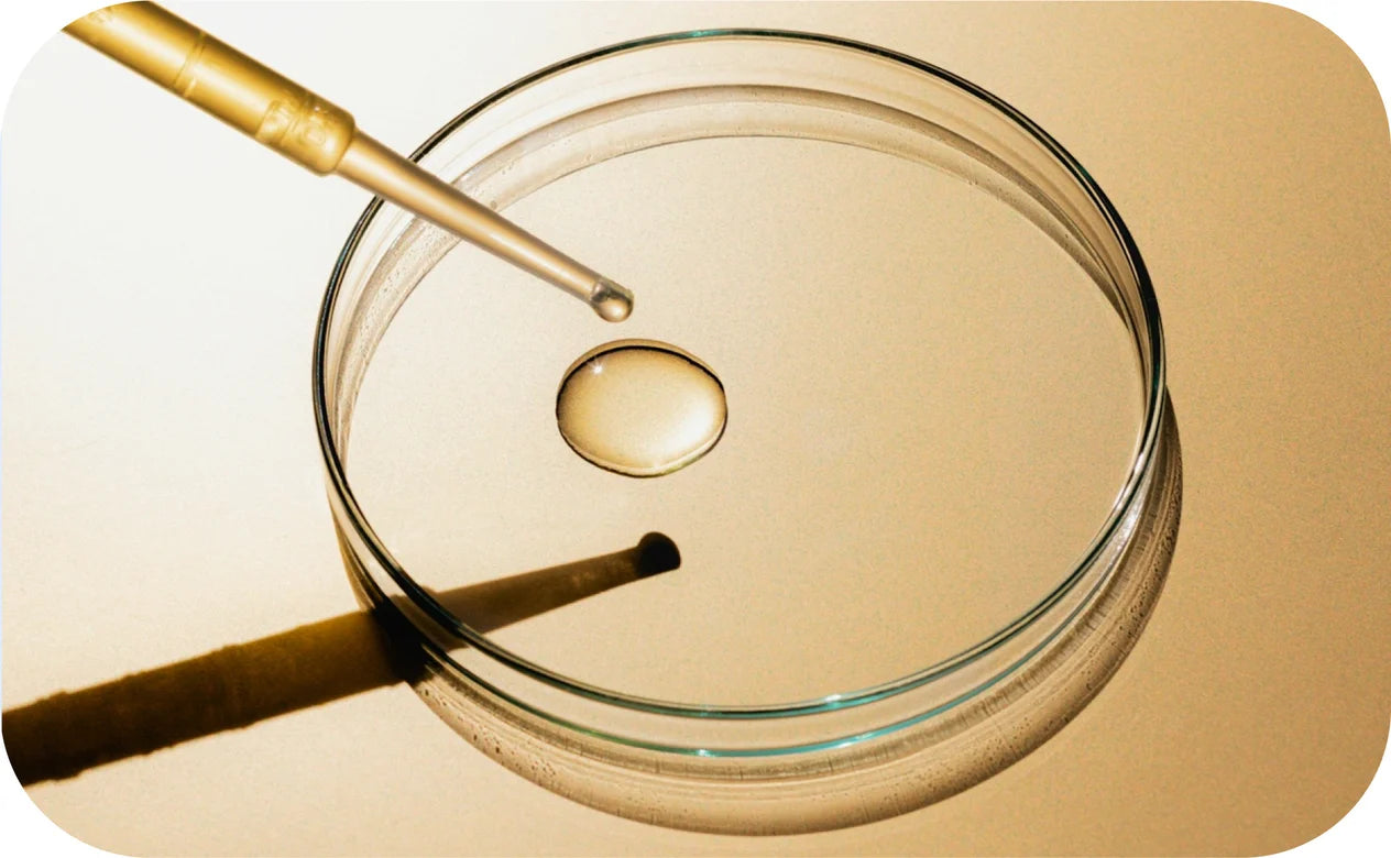 Glass container with a droplet of oil and a wooden tool on a beige background