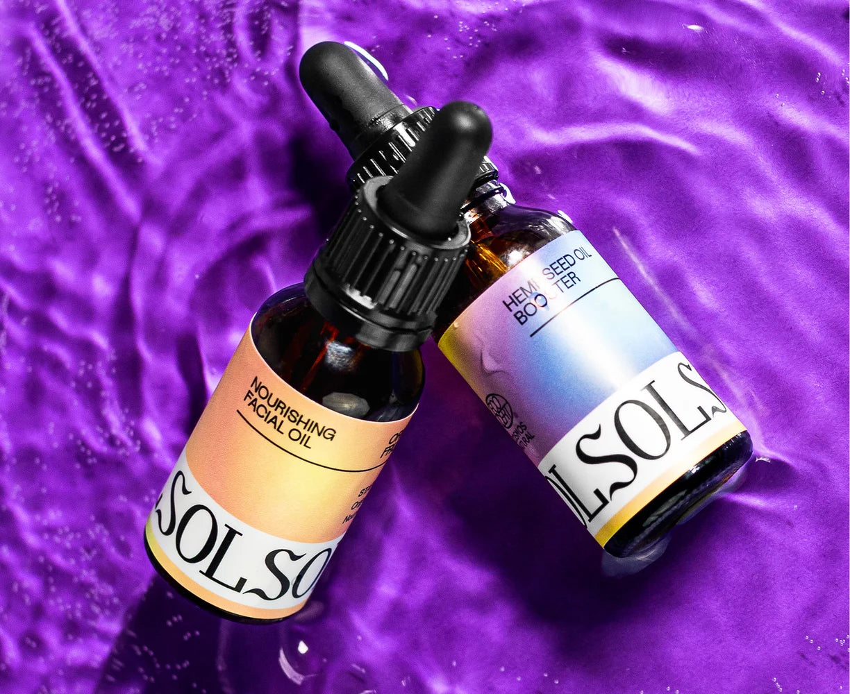 Two bottles of facial oil on a purple textured background